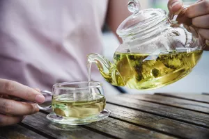 Hands pouring a glass kettle of green tea