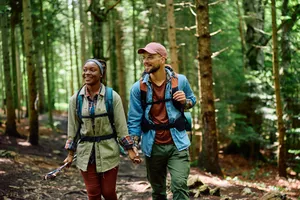 Couple rucking in the woods with rucksacks holding hands.