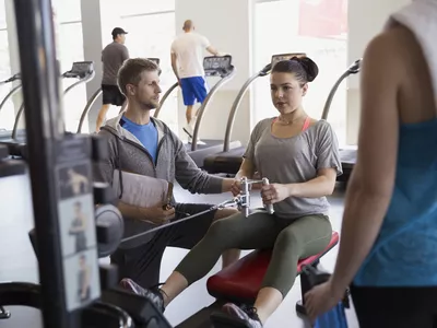 Personal trainer guiding woman seated cable row gym