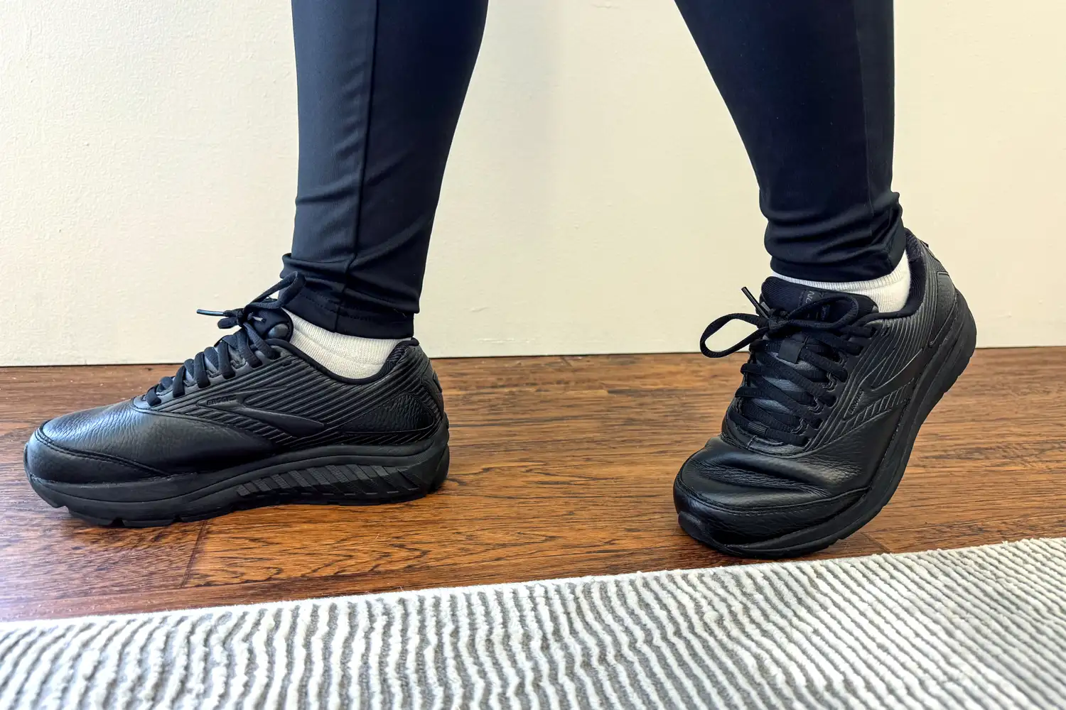 A person wearing Women's Addiction Walker 2 Sneakers with leggings standing on a wooden floor near a rug