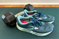 A pair of sneakers placed next to a dumbbell on an exercise mat