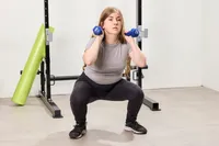 A person squats while holding the JFIT Dumbbell Set with Rack