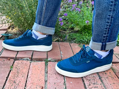 A person wears the Kizik Men's Prague 2 Sneakers while walking on brick outside