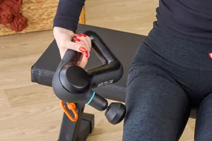 Person holding a massage gun near their leg on a bench.