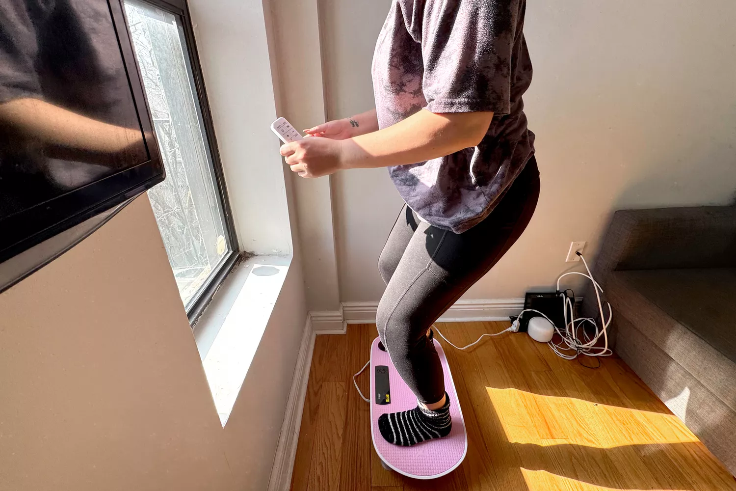 A person squats while standing on the Merach Whole Body Vibration Plate