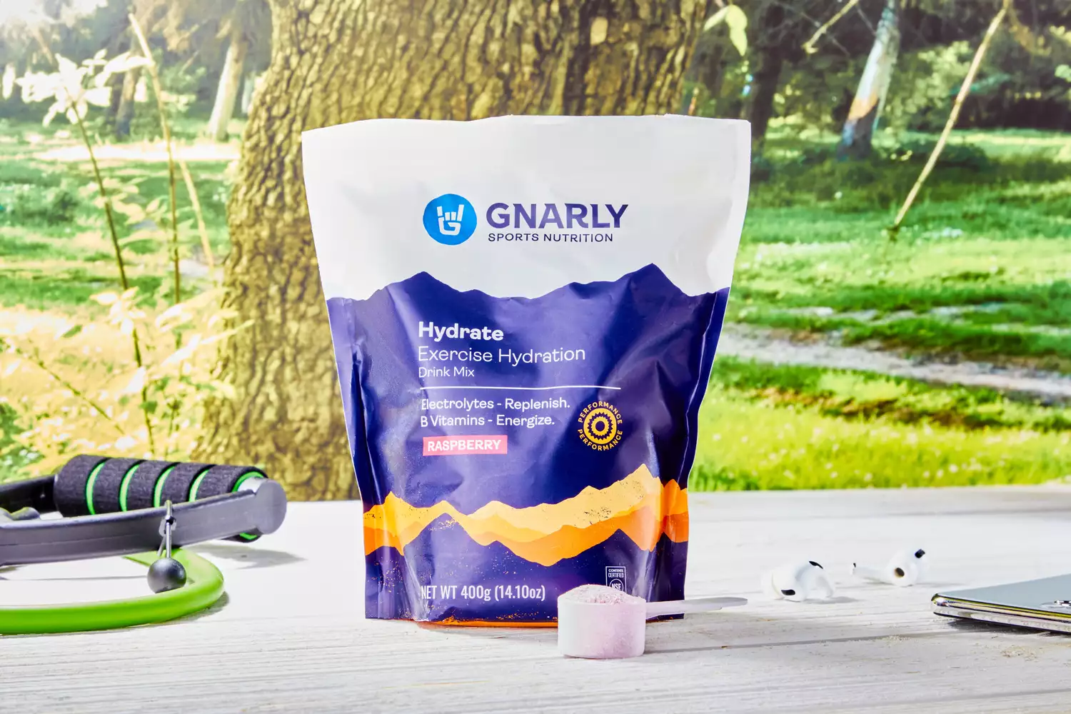Gnarly Nutrition Hydrate Electrolyte Powder in a scoop on a wooden table next to its packaging and props