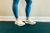 Legs wearing sporty shoes and leggings on a mat against a wall