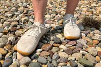 A person rocks on rocky ground while wearing the Vivobarefoot Women's Primus Lite Knit Natural Sneakers