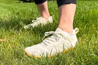 A person wears the Vivobarefoot Women's Primus Lite Knit Natural Sneakers on grass
