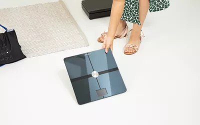 Person picking up Withings Body Comp Smart Scale from floor